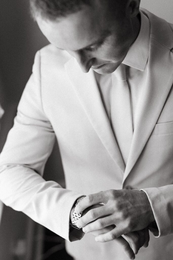 black and white portrait of the groom putting on his watch on his wedding day